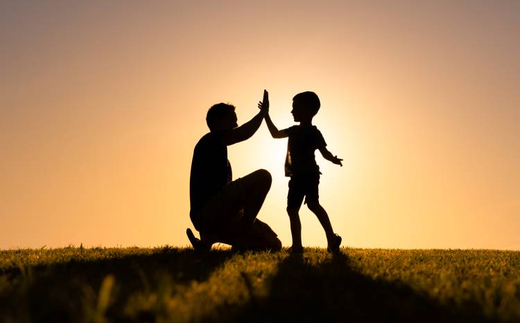 a father raising a boy high five at sunset silhouette