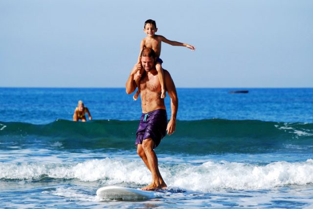 dad surfing with son on shoulders family vacation
